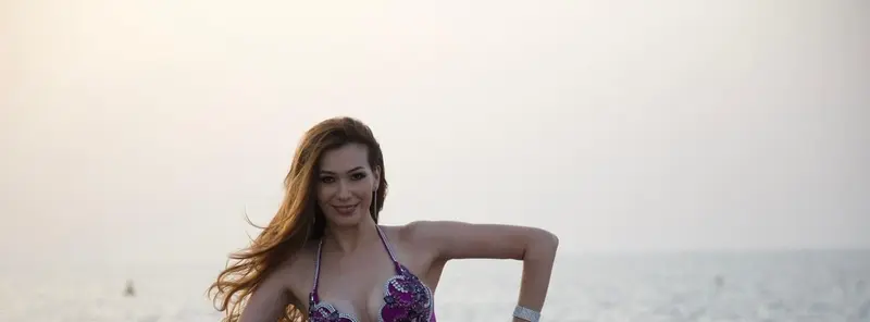 Belly dancer CR posing on rocks by the sea at sunset