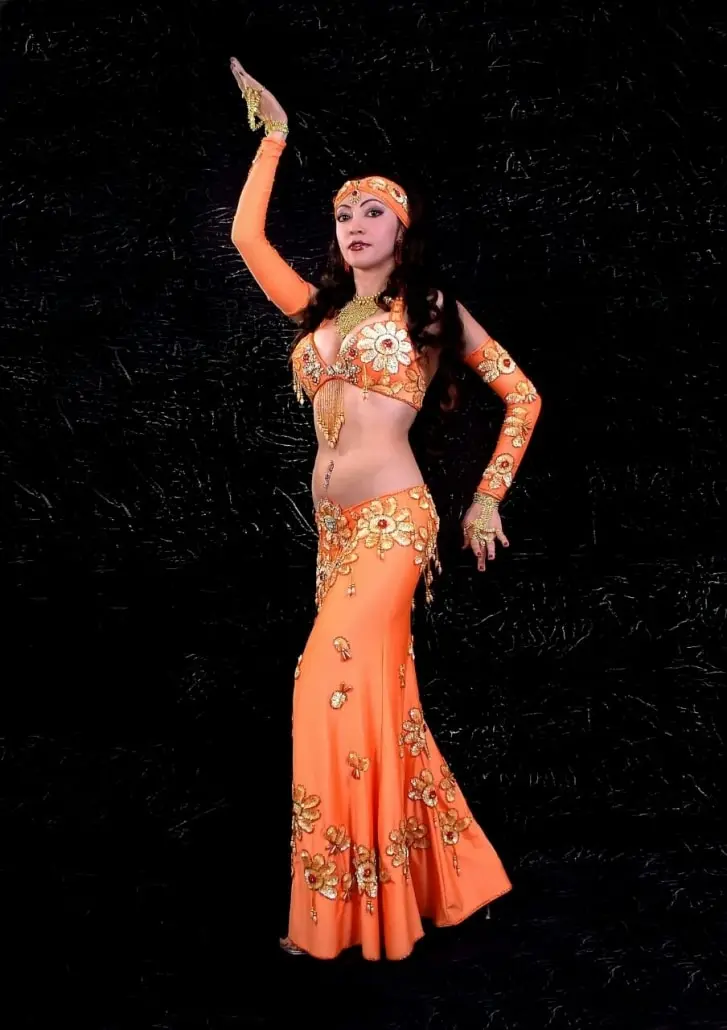 Belly dancer M in an orange costume against a black background