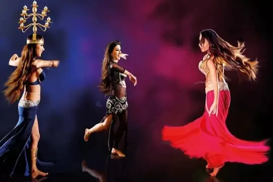 Three belly dancers on stage, one balancing a candelabra on her head
