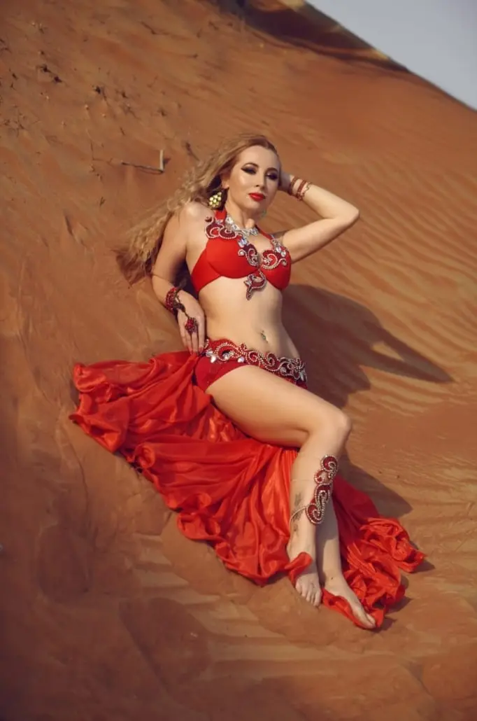 Xena, belly dancer, in a red costume on desert sand