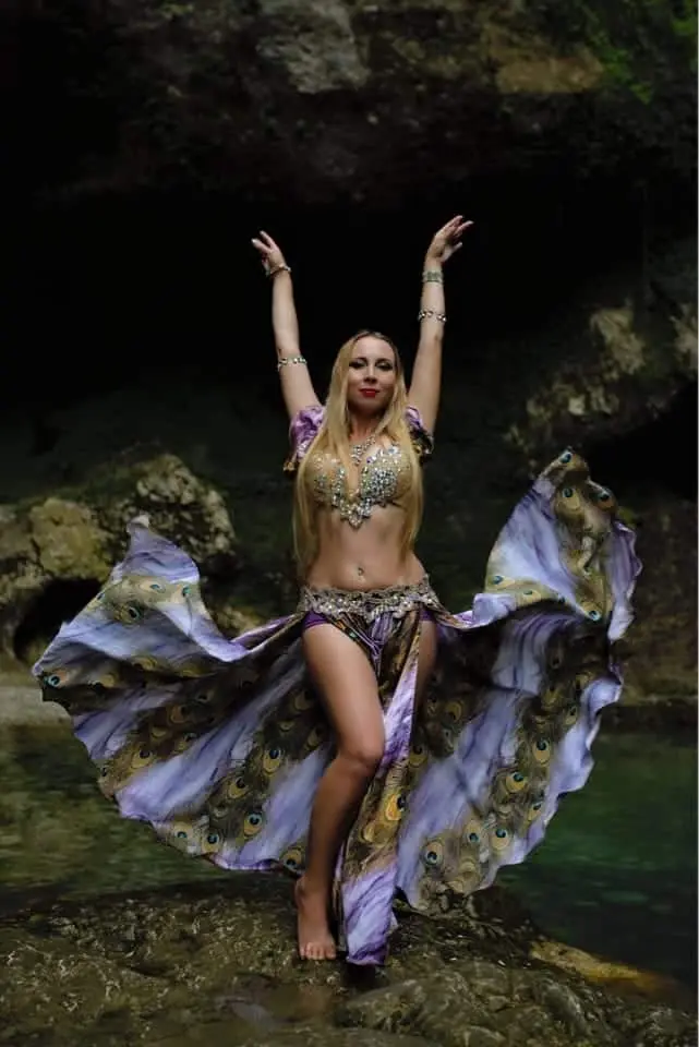 Xena, belly dancer, with a peacock print skirt by a rock pool